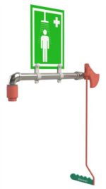 The Justrite H emergency shower station features a green and white sign with a red showerhead icon and first aid symbol. Its metal pipe structure has a red pull lever, labeled Shwr, for rapid response in emergencies. Product: Justrite H, Shwr, Rng Mn Mnt W/O Plt, Ss.