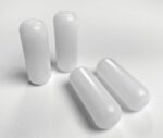 Four white plastic caps, resembling the minimal design of Justrite Poly Shelf/Pegs 24010 & 24015, sit on a white surface. Two stand upright while two lie sideways, highlighting their cylindrical shape with rounded tops and flat bases.