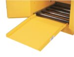A close-up of a yellow industrial machine shows a Justrite Drum Ramp, F/All Drum Cabinets extending outward. The ramps textured surface complements the machine’s interior lined with metal rollers for efficient operation.