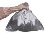 Someone uses a yellow plastic tie to secure a Justrite Smokr Bucket Liner from a pack of 10. The metallic gray bag, featuring printed images or symbols, is skillfully handled to ensure contents remain secure.