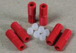Red, threaded plastic anchors and small white caps from the Justrite 3.0 Mm Tubing Connector Set are neatly arranged on a textured surface with six red anchors and eight white caps evenly spaced.
