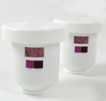 The Justrite Filter, Clr Crtrdg, 2Pk, Aerslv features two white cylindrical containers with small windows displaying pink beads inside. Each container has READY and REPLACE indicators in matching pink on a pristine white background.