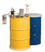 A yellow Dual Comp Sys drum holds equipment and a booklet, with cables and a small metallic device attached, placed beside a blue drum featuring a white cap.