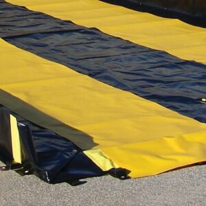 The yellow and black Justrite Track Runner, measuring 3X10, rests on concrete. Designed for outdoor use, it boasts sturdy edges and textured fabric. Small clips hold it securely in place, emphasizing its safety features.