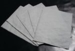 Five sheets of paper, similar to the quality of Justrite Pad Drip Refills 21X23, are fanned out on a dark surface, with lighting accentuating their texture and slight translucency.