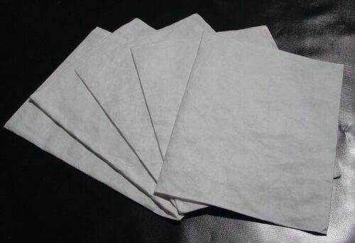 Five sheets of paper, similar to the quality of Justrite Pad Drip Refills 21X23, are fanned out on a dark surface, with lighting accentuating their texture and slight translucency.