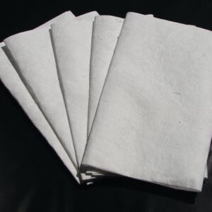 Several sheets resembling pages from a Justrite Pad, Drip Ext Refills 24X36 are fanned out and neatly arranged on a dark surface, highlighting their texture and clean appearance.