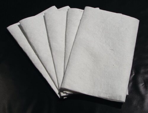 Several sheets resembling pages from a Justrite Pad, Drip Ext Refills 24X36 are fanned out and neatly arranged on a dark surface, highlighting their texture and clean appearance.