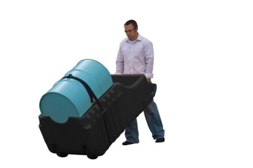 A person in a light shirt and jeans carefully pushes a Justrite Caddy, Drum, Indr/Outdr Eco Bk, angled to secure two blue barrels with a strap against a plain white backdrop.