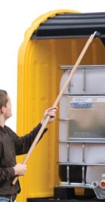Using the Justrite IBC Outdoor Shed Reach Pole, a person opens a yellow containers lid, revealing a large white plastic storage tank with a front metal plate. The plain white background highlights the scenes simplicity.