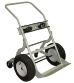 The Justrite Gcyl Ht,2Cyl,4W,Fpt,16 hand truck features a sturdy metal frame, large rubber wheels, and a flat base for carrying items. It includes handles for easy maneuvering and small pivoting wheels at the back for added support and stability.