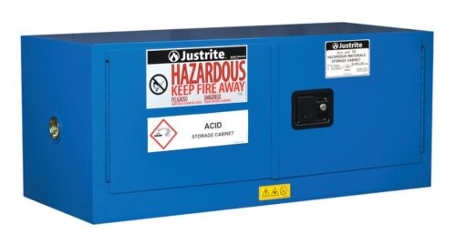 The blue Justrite Cabinet, Haz Mat Pigybk 12G Sc, is designed for acid storage and features warning labels like Hazardous Keep Fire Away. It includes two doors, a lockable handle, and hazard symbols against a white background.