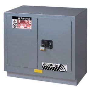 A gray metal Justrite Cabinet Fmhd 23G/36 Man Slv with two padlocked doors is labeled Flammable Keep Fire Away and features safety symbols, with black and white striped warning labels at the bottom for extra caution.