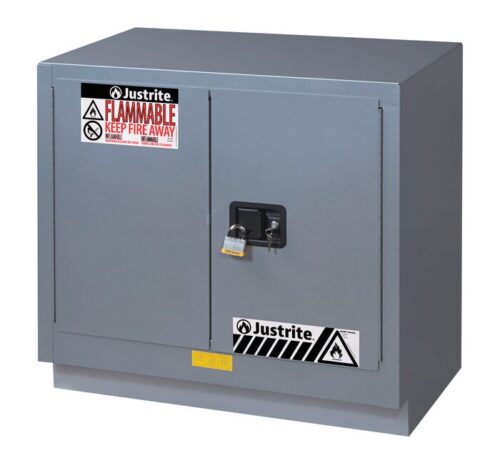 A gray metal Justrite Cabinet Fmhd 23G/36 Man Slv with two padlocked doors is labeled Flammable Keep Fire Away and features safety symbols, with black and white striped warning labels at the bottom for extra caution.
