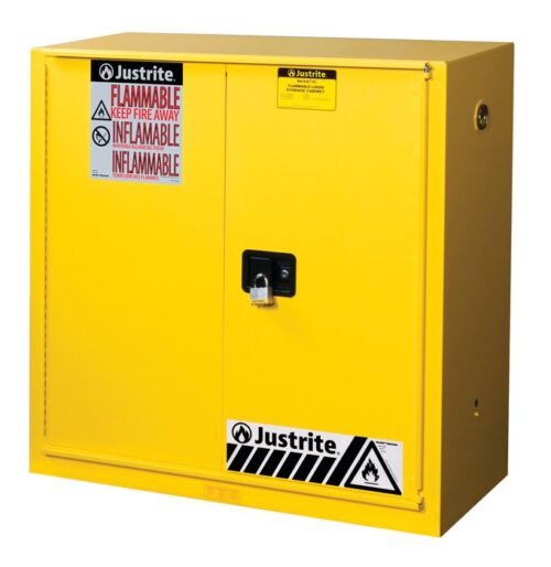 The yellow Justrite Cabinet, model Flam 30G, Sc/Bifld Yl, has two doors with a black handle on the right door secured by a padlock. Red and white FLAMMABLE KEEP FIRE AWAY labels are prominently displayed alongside caution signs near the base.