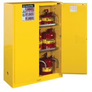 A yellow Justrite Cabinet, Flam Sfty 45G Sc Yel, holds red containers labeled flammable. The sign Flammable Keep Fire Away is in English and Spanish. Its open door reveals three shelves with neatly arranged containers.