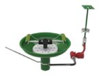 A 3D render shows a green Justrite H,Efwsh,Lb,Tblmt,Opn Ss Bwl,Ss safety shower and eyewash station with chains, foot pedal, piping, showerhead on a vertical pipe, and a red lever.