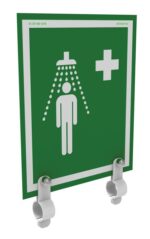 The Justrite H Ssaccy shower sign in green displays a white figure under a showerhead with water droplets and a cross in the top right, mounted on a wall using two white brackets.