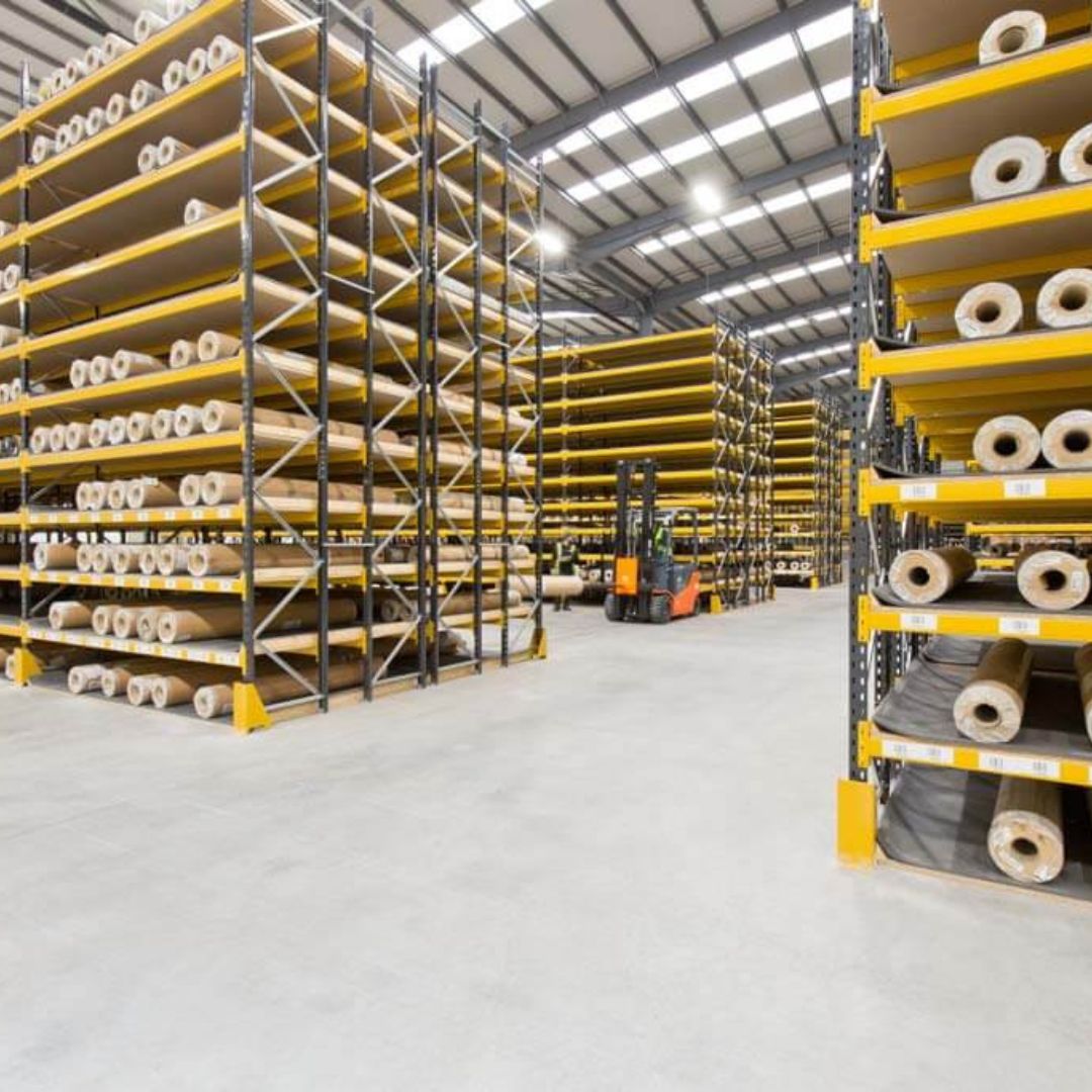 Warehouse aisle of racking filled with rolls of carpet and vinyl with a forklift working