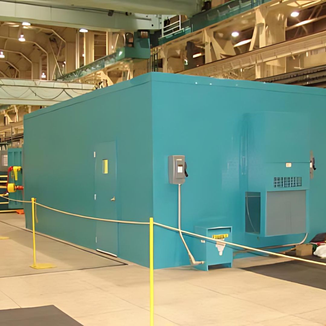 A spacious, turquoise-colored machine enclosure located indoors, equipped with large HVAC systems. It has a modern design with clean lines, multiple doors, and access panels, indicating its use in a controlled environment within a facility.