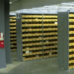 Metal shelving in a warehouse, filled with yellow-labeled bins organized meticulously, demonstrating an efficient inventory management system.