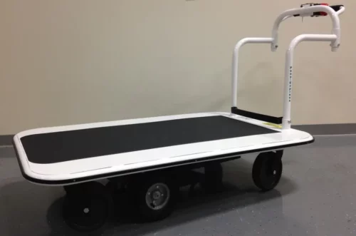A white flatbed cart with black wheels and a curved handle features a black non-slip platform. With a 3000 lb. capacity, it stands on a gray speckled floor by a light wall, set to tackle tasks like the Electro Kinetic Technologies Pony Express Motorized Platform Truck.