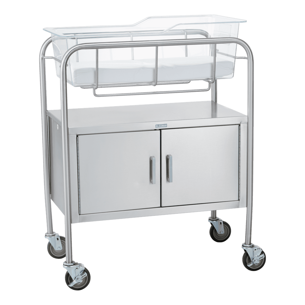 The Blickman stainless steel hospital bassinet features a clear plastic cradle and a lower cabinet with double doors, all set on four wheels for easy mobility.