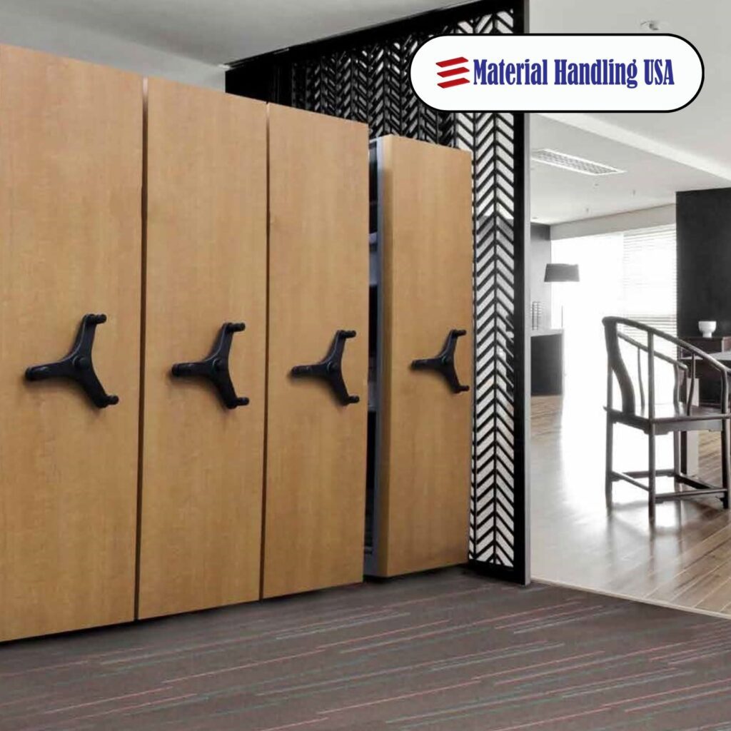 A modern office showcases large, movable wooden storage units with black handles, complemented by stylish Aurora Shelving. In the background, a table with chairs and a patterned partition feature prominently. The logo Material Handling USA is displayed at the top right corner.
