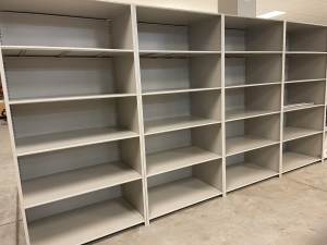 A large, empty shelving unit reminiscent of those used in the Utah Museum, featuring five columns and three rows of light-colored wood. It stands on a gray concrete floor with evenly spaced shelves, ready for storage or display against an off-white wall.