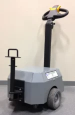 The Electro Kinetic Technologies Pony Express Electric Tugger features a 5000-pound capacity, a round bar hitch, two wheels, a vertical handlebar with control panel, and an under-mounted stabilizing wheel for smooth floor navigation.