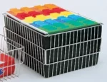 A metal filing basket, similar to those used in the Electro Kinetic Techs. Pony Express Cart (Part MMC-SM01), holds several black folders with orange, yellow, blue, and green tabs. It sits against a neutral backdrop with another basket partially visible on the left.
