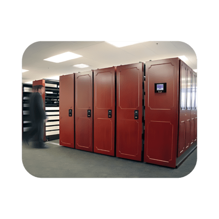 A person walking past a row of large, red server cabinets akin to mobile high density shelving systems in a well-lit room. The cabinets feature digital screens and handles, while the blurred motion effect captures the persons swift movement.