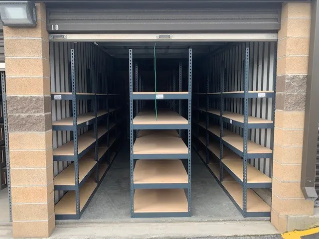 Empty archive shelving for law firms is neatly lined up inside a small storage unit with a partially open door. The unoccupied shelves reveal the interior of the concrete block space, visible from the outside.