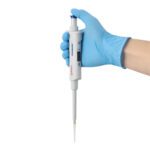 A hand in a blue glove holds the MH-USA Precipette Pipette, equipped with a digital display and adjustable volume of 10-100μl. Its pointed tip ensures precise liquid measurement and dispensing, making it perfect for accurate lab work.