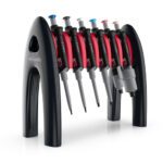 A set of seven red and black laboratory pipettes with colorful tips are neatly arranged on an MH-USA Per4mance Pipette Stand, 6-Slot Rack, Black, creating a visually appealing display of scientific equipment.