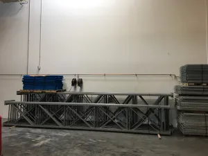 A warehouse interior features sturdy metal scaffolding and frames against a blank wall, ideal for pallet rack solutions in auto glass distribution centers. Blue folded tarps sit atop the structures, with metal sheets neatly stacked on the right. The concrete floor completes the efficient setup.