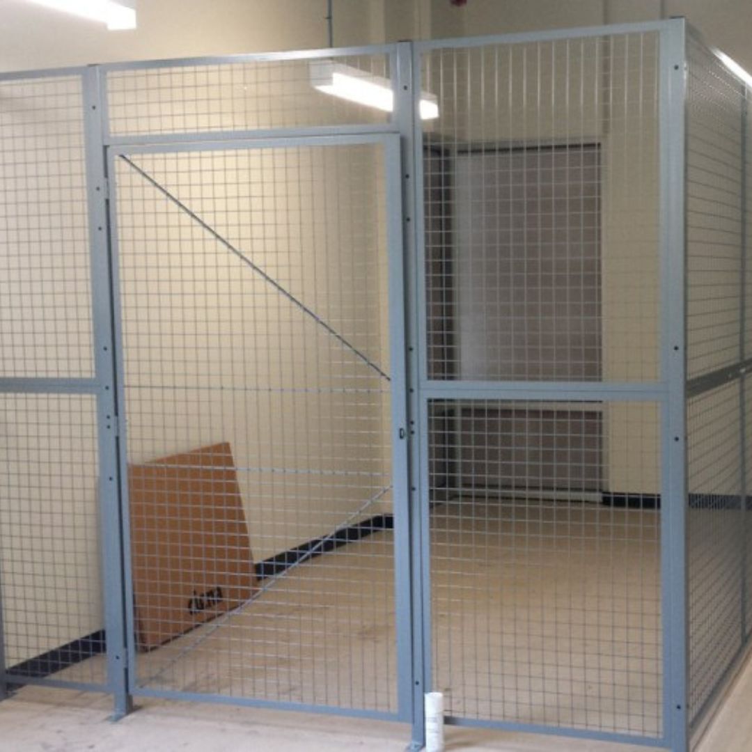 Grey welded wire mesh partition enclosure with a hinged door forming a secure storage room
