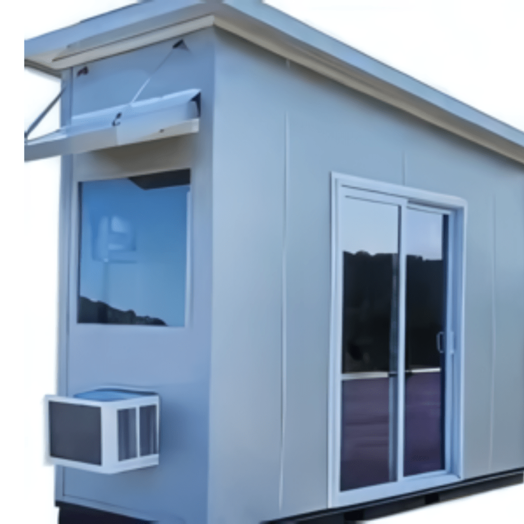 A small, modern ticket booth with a modular prefab design features a light gray exterior. It boasts sliding glass doors and a large window with an awning, complemented by a rectangular air conditioning unit mounted below the window for comfort.