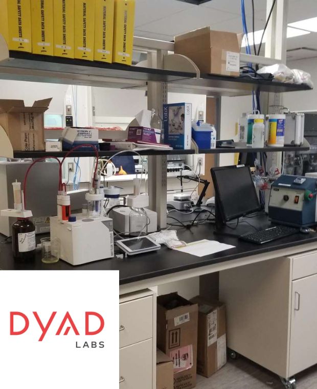 The Dyad Labs workspace, bustling with scientific equipment and a laptop on the countertop, reflects a seamless blend of organization. Shelves are lined neatly with supplies and instruments. As part of our lab renovation services, boxes and containers add to the efficient layout.