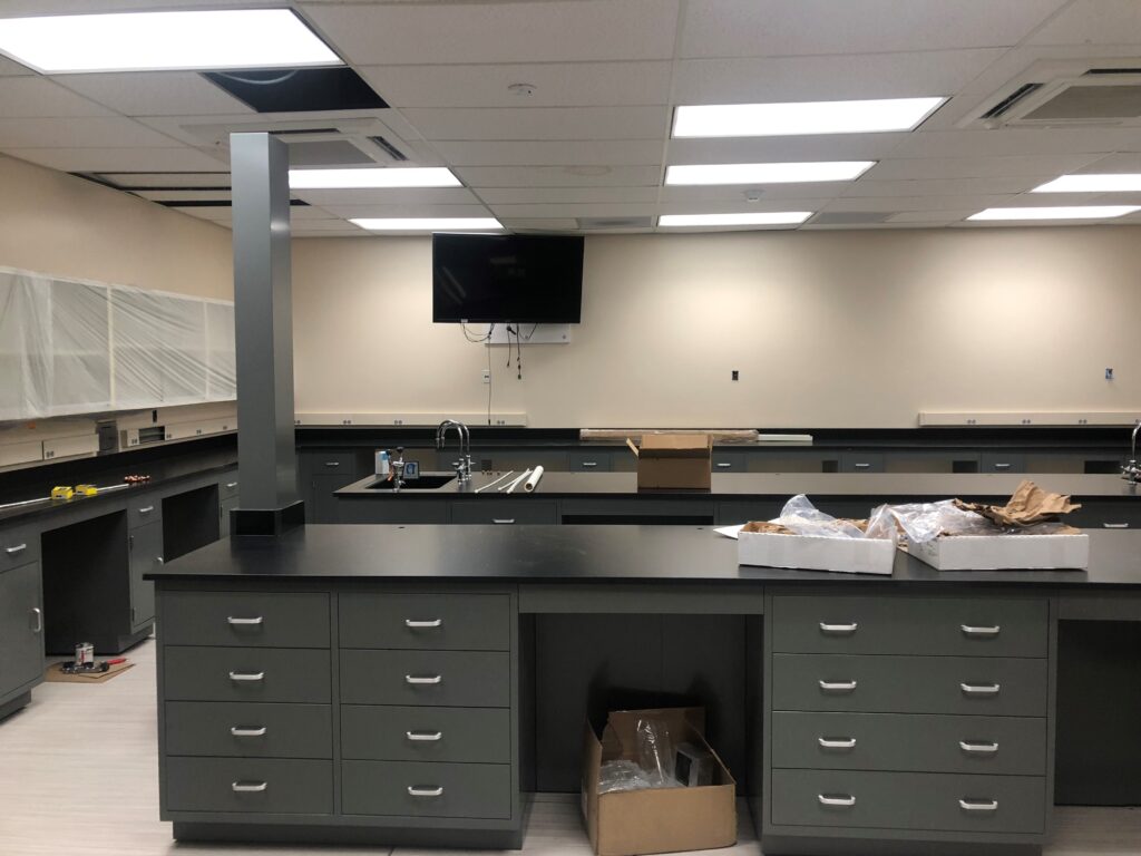The science laboratory at Weber State University boasts black countertops, grey cabinets, and ceiling lights. A flat screen monitor is mounted on the wall. Boxes and packing materials strewn about hint at ongoing installation in this state-of-the-art facility.