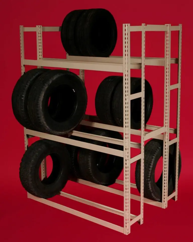 A beige metal shelving unit, a prime example of Storage Solutions with BASC, holds multiple black tires against a solid red background. The neatly organized shelves display rows of tires, highlighting efficient organization.