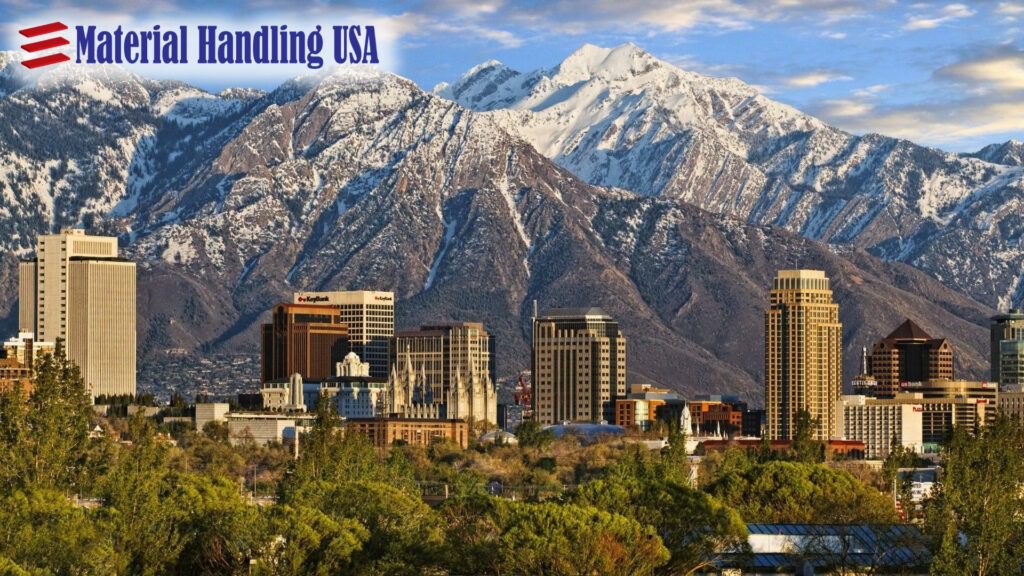 City skyline with tall buildings set against snow-capped mountains under a partly cloudy sky. The logo Material Handling USA appears in the upper left corner, highlighting our case studies and innovations in urban landscapes.