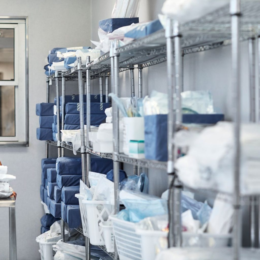 In the well-organized medical storage room, reminiscent of a meticulously managed department warehouse, shelves are stocked with various medical supplies and equipment, featuring neatly stacked blue packages and white containers.