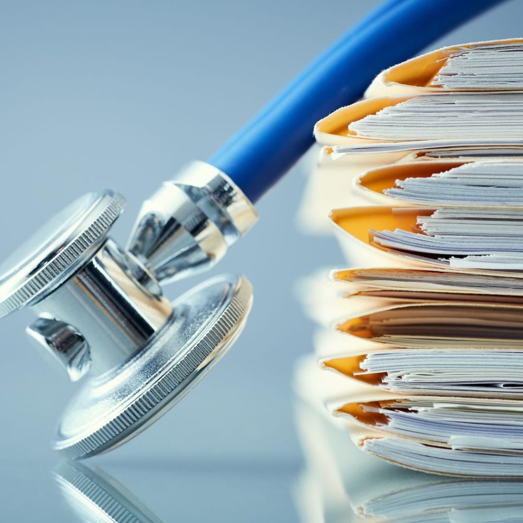 A stethoscope rests against a stack of thick folders, neatly organized with yellow covers, symbolizing healthcare documentation and medical records against a blue-gray background.