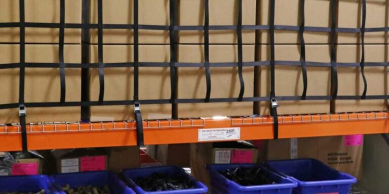 Warehouse shelving loaded with cartons secured behind warehouse safety netting
