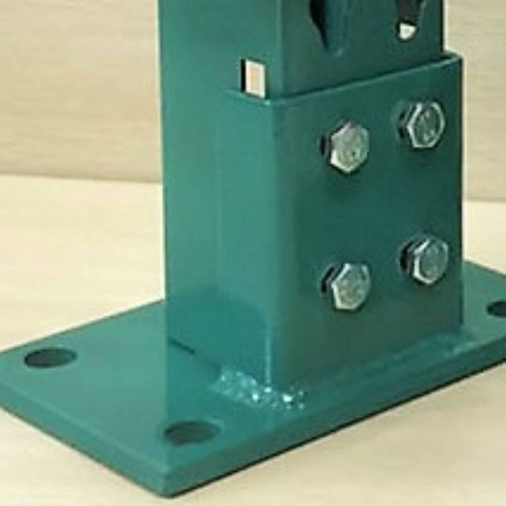 A close-up image of a green metal base with four bolts securing it, positioned on a flat surface, typical of an industrial shelving solution. The base has multiple openings for adjustable fittings and is attached to a flat plate with holes on the corners.