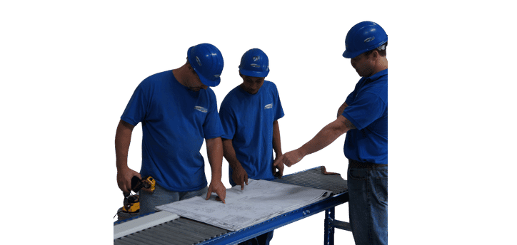 Three dedicated installers in blue shirts and helmets stand around a table, intensely focused on a blueprint. One of them grips a power drill, ready to bring the plans to life. This image captures their commitment and teamwork in action.