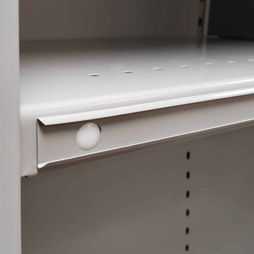 Close-up of a metal storage shelving unit with a smooth, light gray finish. The shelf features small circular holes along the edge and an inset round white peg. Vertical slots on the side allow for adjustable shelving, making it ideal for industrial shelving solutions.