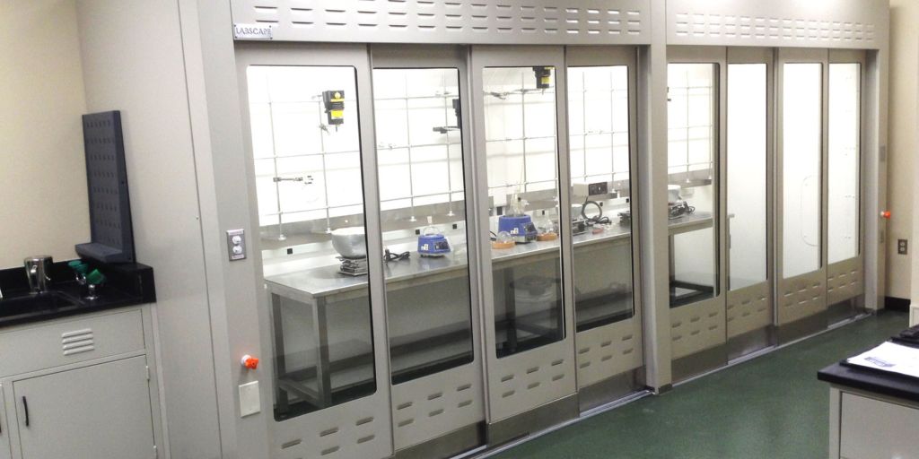 Row of walk-in fume hoods with full-height sashes along a laboratory wall