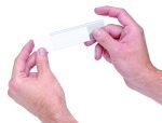 Two hands hold a clear microscope slide against a white background, fingers grasping gently on either side. It demonstrates precision akin to Quantum Label Holders with laser label inserts (25 per pack), underscoring meticulous attention to detail.